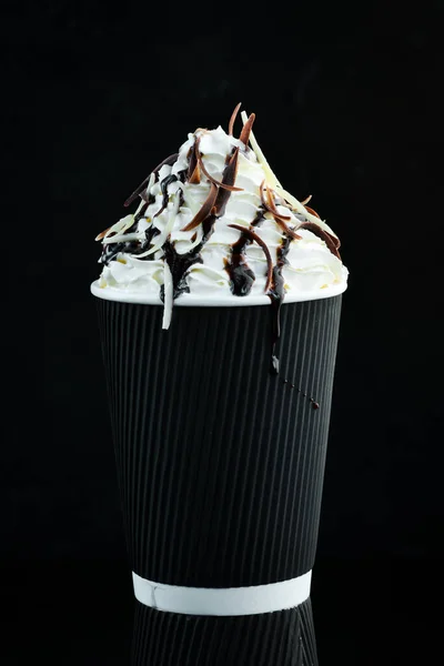 Coffee with chocolate and cream in a paper cup. on a black background. Free space for text.