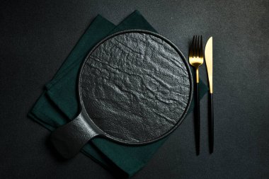 Gold knives and forks on a black background, empty black plate. Beautiful gold cutlery. View from above.
