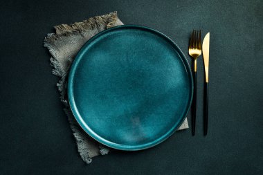 Gold knives and forks on a black background, empty black plate. Beautiful gold cutlery. View from above.