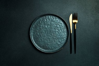Gold knives and forks on a black background, empty black plate. Beautiful gold cutlery. View from above.