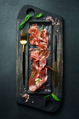 Siyah taş bir tabakta jambon dilimleri. Karanlık bir arkaplanda, yakın plan.