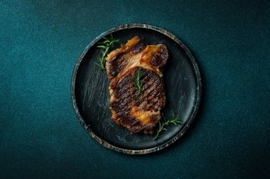 Ahşap tabakta baharatlı ızgara biftek. Koyu mavi taştan bir arka planda. Üst görünüm.