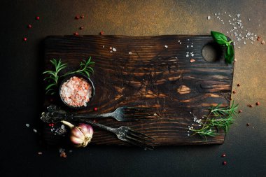 Kesme tahtası, biberiye ve baharatlar. Karanlık bir arka planda. Tarif için boş alan.