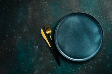 Mavi tabak ve çatal bıçak takımı. Koyu yeşil turkuaz bir arka planda. Metin için boş alan.