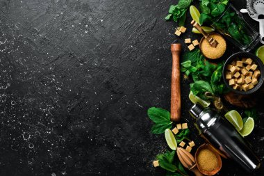 Mojito hazırlığı: karıştırıcı, limon, nane ve buz. Siyah taştan bir arka planda. Üst görünüm.