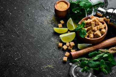 Kokteyl hazırlığı. Bar sayacı: karıştırıcı, limon, nane ve buz. Siyah taştan bir arka planda Mojito. Üst görünüm.