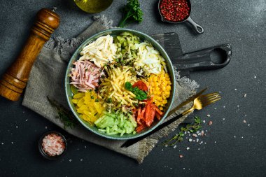 Salatalık, kırmızı biber, domates, patates ve haşlanmış sosisten yapılmış renkli sebze salatası. Karanlık bir taş arka planda.