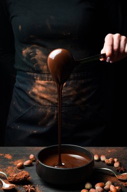 Şef sıcak çikolatayı bir kaseye boşaltıyor. Siyah bir arka planda. Çikolata hazırlığı.