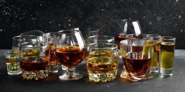 Votka, konyak, tekila, viski, brendi ve viski, grappa, likör, vermut, tentür, rom gibi çeşitli alkollü içeceklerle dolu bardaklar. Sert alkollü içecekler. Taş bir arka planda.