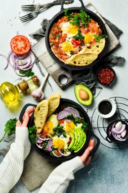 Ispanak, avokado, kızarmış ekmek ve domatesli Shakshuka yumurtası tutan kadın elleri. Baharatlı domates soslu haşlanmış yumurta..