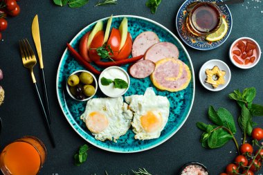 İngiliz kahvaltısı. Kızarmış yumurta, salam, pastırma ve sebze. Çay ve tatlı. Koyu bir arkaplanda.