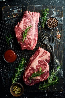 Baharatlı iki çiğ kaburga bifteği. Metin için boş alan. Siyah taştan bir arka planda.