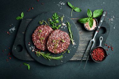 Baharatlı hamburgerli köfte ve tahta tabakta otlar. Karanlık bir taş arka planda. Üst görünüm.