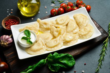 Beyaz kare tabakta, patates ve ekşi kremalı Ukrayna hamur tatlısı. Metin için boş alan. Karanlık bir arka planda.