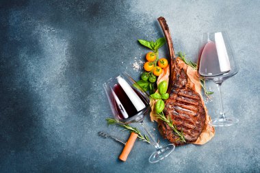Bardakta şarap ve kemikte ızgara biftek. Gri beton arka planda. Metin için boş alan. Üst görünüm.