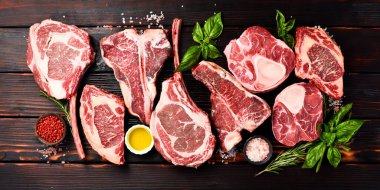 Baharatlı ızgara için çiğ biftek çeşitleri: Tomahawk bifteği, Ribeye, Ossobuco ve T-bone bifteği, ahşap kahverengi arka planda..