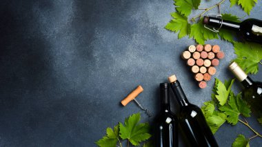 Arka planda üzüm yaprakları, tirbuşon ve şarap mantarları olan bir şişe şarap. Gri beton bir yüzeyde.
