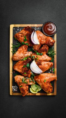 Tahtada soğan ve baharatla kızarmış tavuk kanadı. Karanlık bir arka planda.