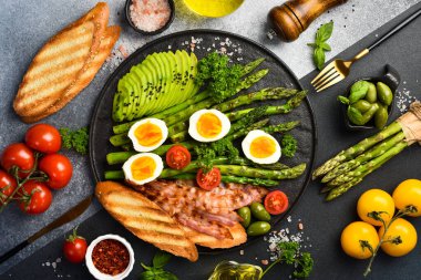 Lezzetli bir kahvaltı. Güneşli tarafı yumurta, kuşkonmaz, pastırma ve avokado. Siyah taştan bir tabakta.