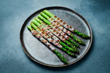 Taş tabakta domuz pastırmalı kızarmış kuşkonmaz. Üst görünüm.