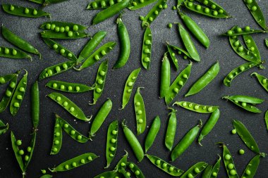 Siyah bir arkaplanda yaprakları olan yeşil bezelyeler. Üst Manzara. Sağlıklı yemek..