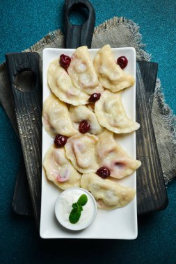 Beyaz kare tabakta vişneli ve ekşi kremalı hamur tatlısı. Metin için boş alan. Karanlık bir arka planda.