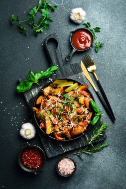 Metal bir tavada sosis ve peynirli kızarmış patates. Karanlık bir arkaplanda, yakın plan.