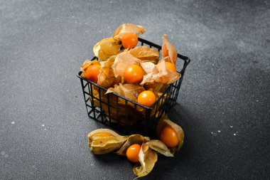 Taze altın sulu kış kirazları, siyah taş bir masanın üzerinde bektaşi üzümü (physalis). Kapat..