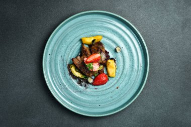 Karamelli elma ve çilekli fırında kaz ciğeri. Siyah taştan bir arka planda. Bir tabakta, yakın plan..