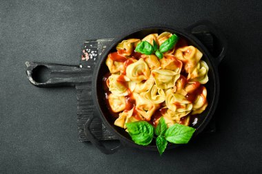 Domates soslu, etli ve fesleğenli geleneksel ravioli. En üstteki görünüm, koyu taştan bir arkaplan.