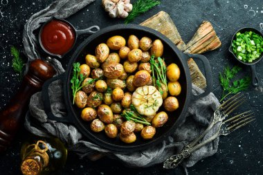 Fırında pişmiş patatesler tavada iştah açıcı. Sarımsaklı, otlu ve baharatlı Rustik fırında patates. Siyah taştan bir arka planda.