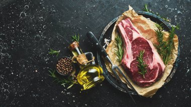 Baharatlı ve biberiyeli çiğ kovboy bifteği. Siyah taş bir masanın üzerinde. Üst görünüm.