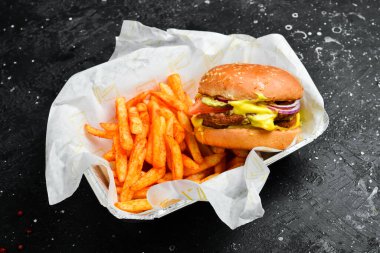 Fast food. Tek kullanımlık tabakta patates kızartması ve hamburger. Tahtada..