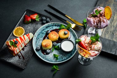 Tatlıların arka planı. Cheesecake, peynirli krep ve dondurma. Siyah taştan bir arka planda.