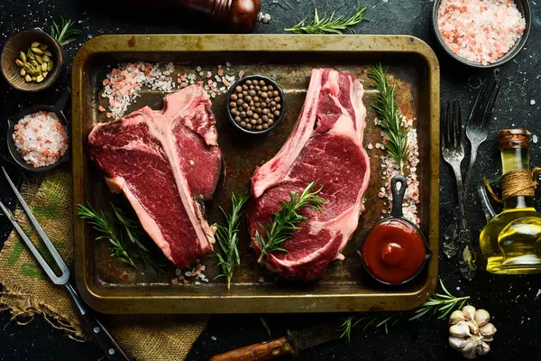 Koyu bir köy tahtasında baharat ve çatal bıçaklarla ızgara yapmak için çeşitli çiğ biftekler.