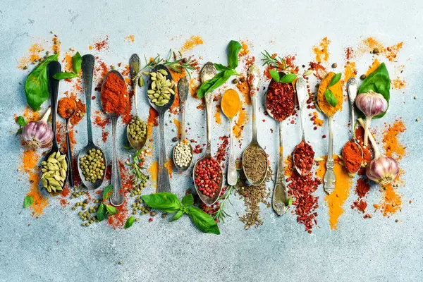 Gri bir arka planda, kaşıklardaki baharatlar ve otlar. Üst Manzara. Metin için boş alan.