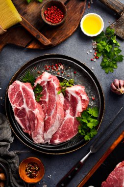 Tabakta baharatlı üç çiğ domuz bifteği. Çiğ et. Gri taştan bir arka planda.