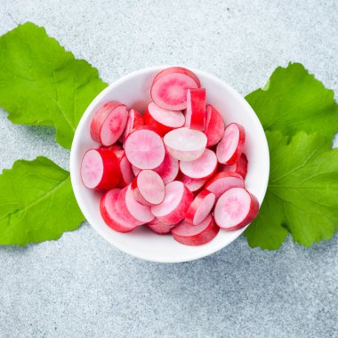 Beyaz bir kasede doğranmış kırmızı turplar. Turp salatası hazırlığı. Gri beton bir arka planda. Kapat..