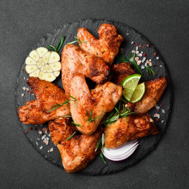 Izgara tavuk kanadı, sarımsaklı ve biberiyeli. Karanlık bir arka planda.