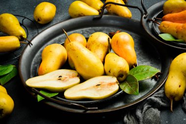 Armutlar tabakta. Kesme tahtasının üzerinde armut dilimleri ve bıçak var. Üst Manzara. Siyah taştan bir arka planda.