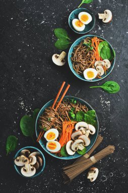 Soba erişteli, yumurtalı, mantarlı ve yeşil soğanlı Asya usulü çorba. Taş zeminde. Üst görünüm.