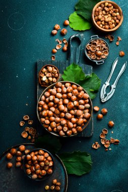 Fındık arka planı. Kasede fındık, fındık kıracağı ve fındık kıracağı. Koyu taş bir masada fındık için maşa. Dikey fotoğraf.