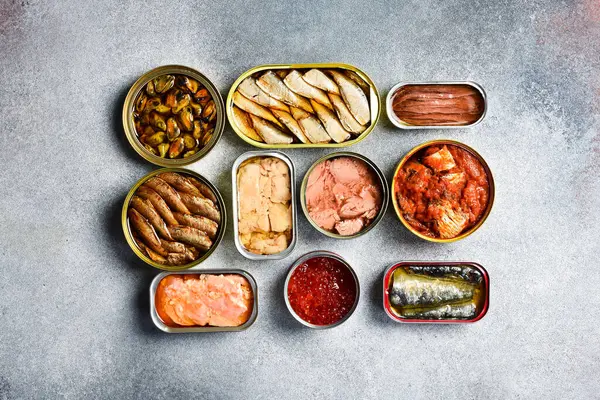 Konserve balık ve deniz ürünleri: ton balığı, somon yumurtası, lahanası, morina ciğeri ve uskumru. Bir ışık taşı arka planında.