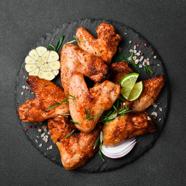 Izgara tavuk kanadı, sarımsaklı ve biberiyeli. Karanlık bir arka planda.