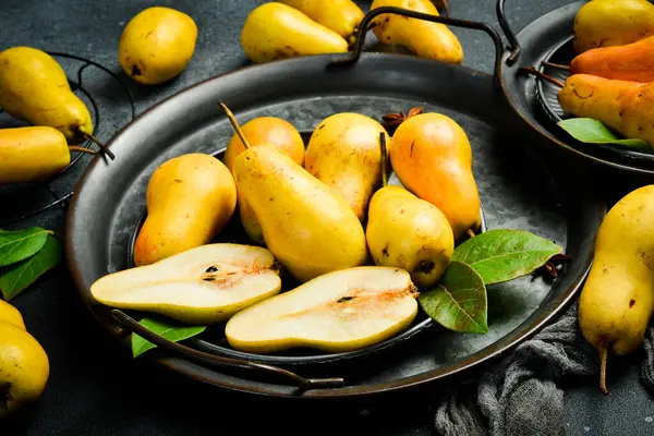 Armutlar tabakta. Kesme tahtasının üzerinde armut dilimleri ve bıçak var. Üst Manzara. Siyah taştan bir arka planda.