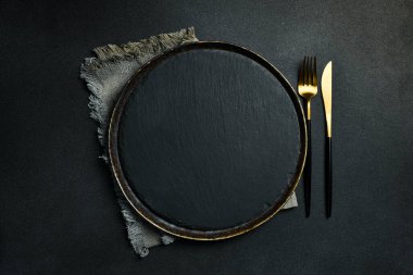 Gold knives and forks on a black background, empty black plate. Beautiful gold cutlery. View from above.