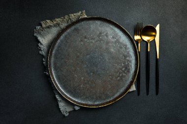 Gold knives and forks on a black background, empty black plate. Beautiful gold cutlery. View from above.