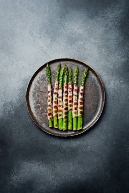 Taş tabakta domuz pastırmalı kızarmış kuşkonmaz. Üst görünüm.