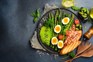 Lezzetli bir kahvaltı. Güneşli tarafı yumurta, kuşkonmaz, pastırma ve avokado. Siyah taştan bir tabakta.