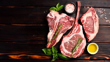 Baharatlı ızgara için çiğ biftek çeşitleri: Tomahawk bifteği, Ribeye, Ossobuco ve T-bone bifteği, ahşap kahverengi arka planda..